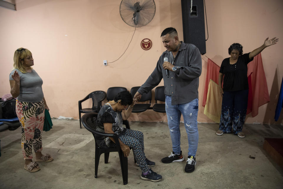 Inmate Jorge Anguilante prays with people at his home in Rosario, Argentina, Saturday, Dec. 4, 2021, as he takes a temporary trip away from the prison where he is serving time. Every Saturday Anguilante heads home for 24 hours to minister at a small evangelical church he started in a garage in Argentina’s most violent city. (AP Photo/Rodrigo Abd)