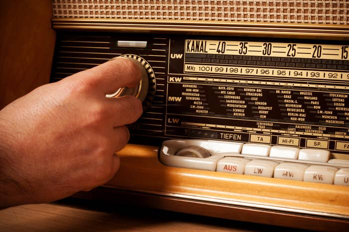 A hand tuning an old-fashioned radio with a wood finish, adjusting the frequency dial on the front panel