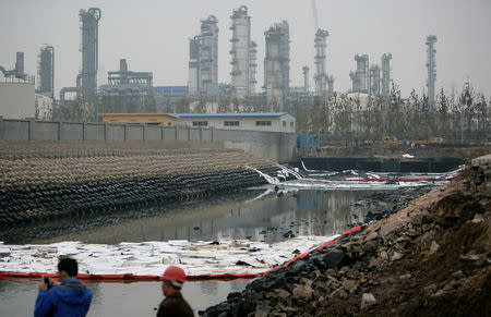 A man takes pictures next to leaked oil after Friday's explosion at a Sinopec Corp oil pipeline in Huangdao, Qingdao, Shandong Province November 23, 2013. REUTERS/Stringer/File Photo