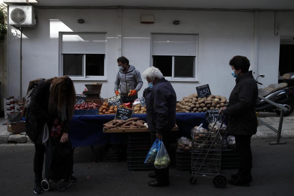 Customers wearing face masks against the spread of coronavirus, wait to buy potatoes at an open-air fruit and vegetable market in Athens, Monday, Nov. 23, 2020. Greece has seen a major resurgence of the virus after the summer, leading to dozens of deaths each day and thousands of new infections. (AP Photo/Thanassis Stavrakis)