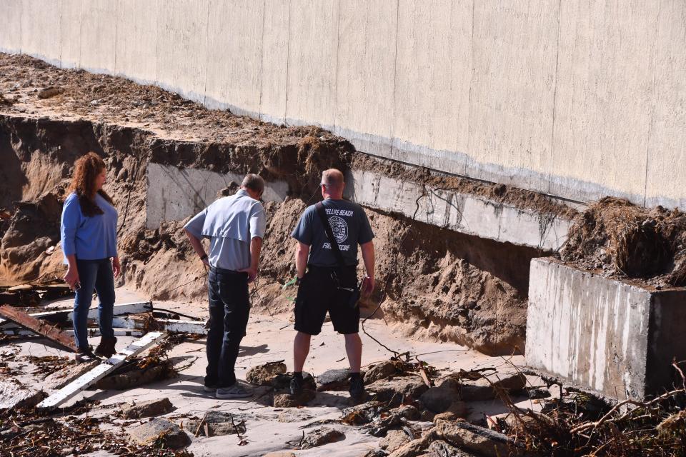 A Satellite Beach Fire Department employee and others look at the base of the Oceana Oceanfront Condominium north tower Friday from the severely eroded beach.