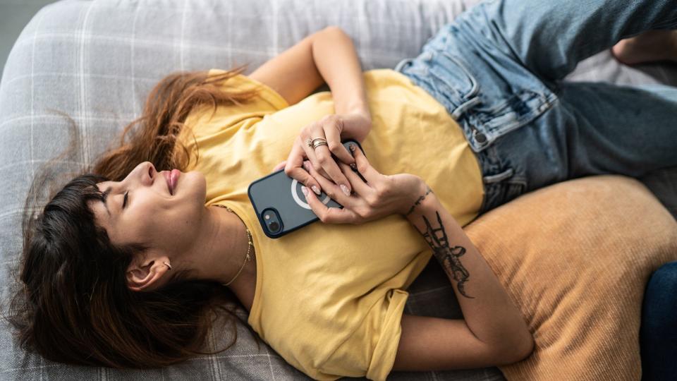 woman lies on bed with a phone held to her heart as she smiles