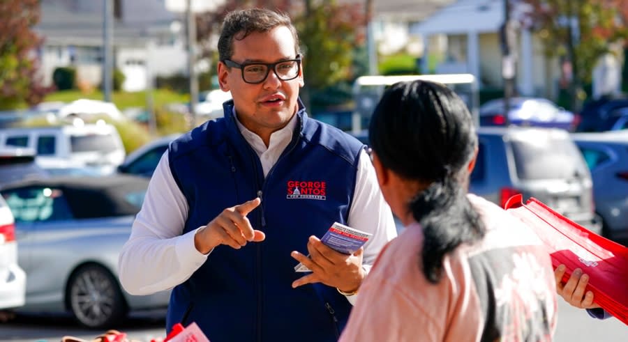 George Santos speaks with a woman while holding campaign materials