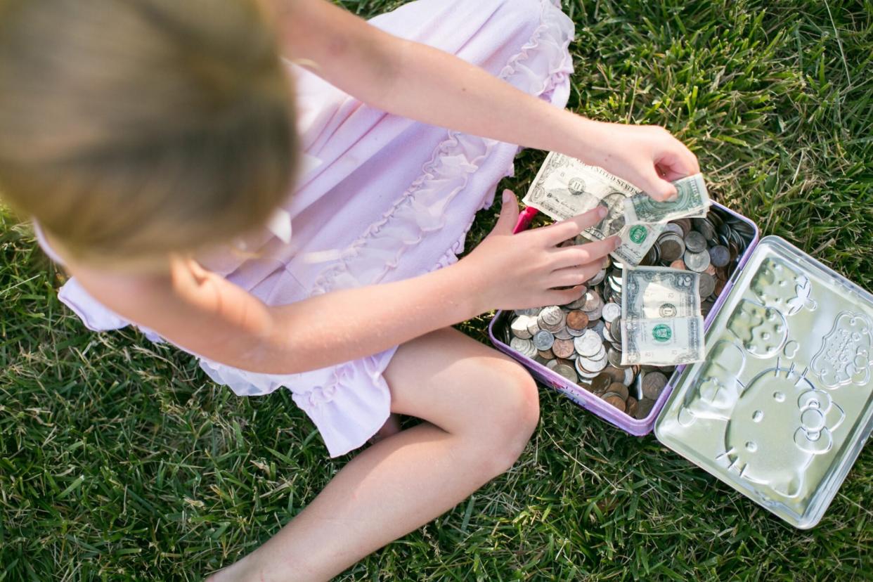 An image of a girl counting dollar bills on the grass.