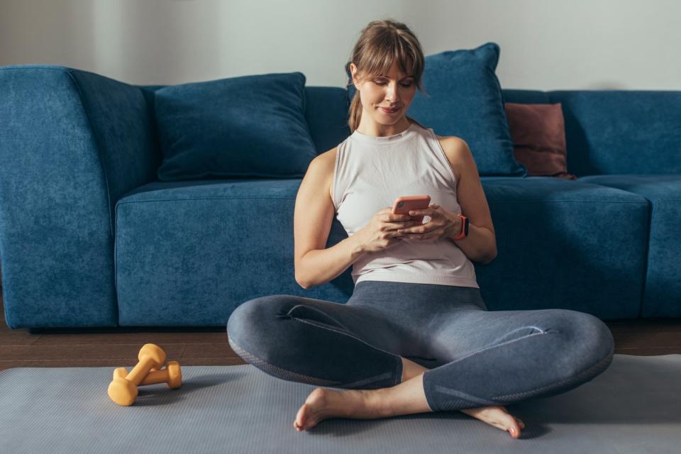 A person wearing an athleisure workout outfit who's seated on the floor next to two dumbbells.