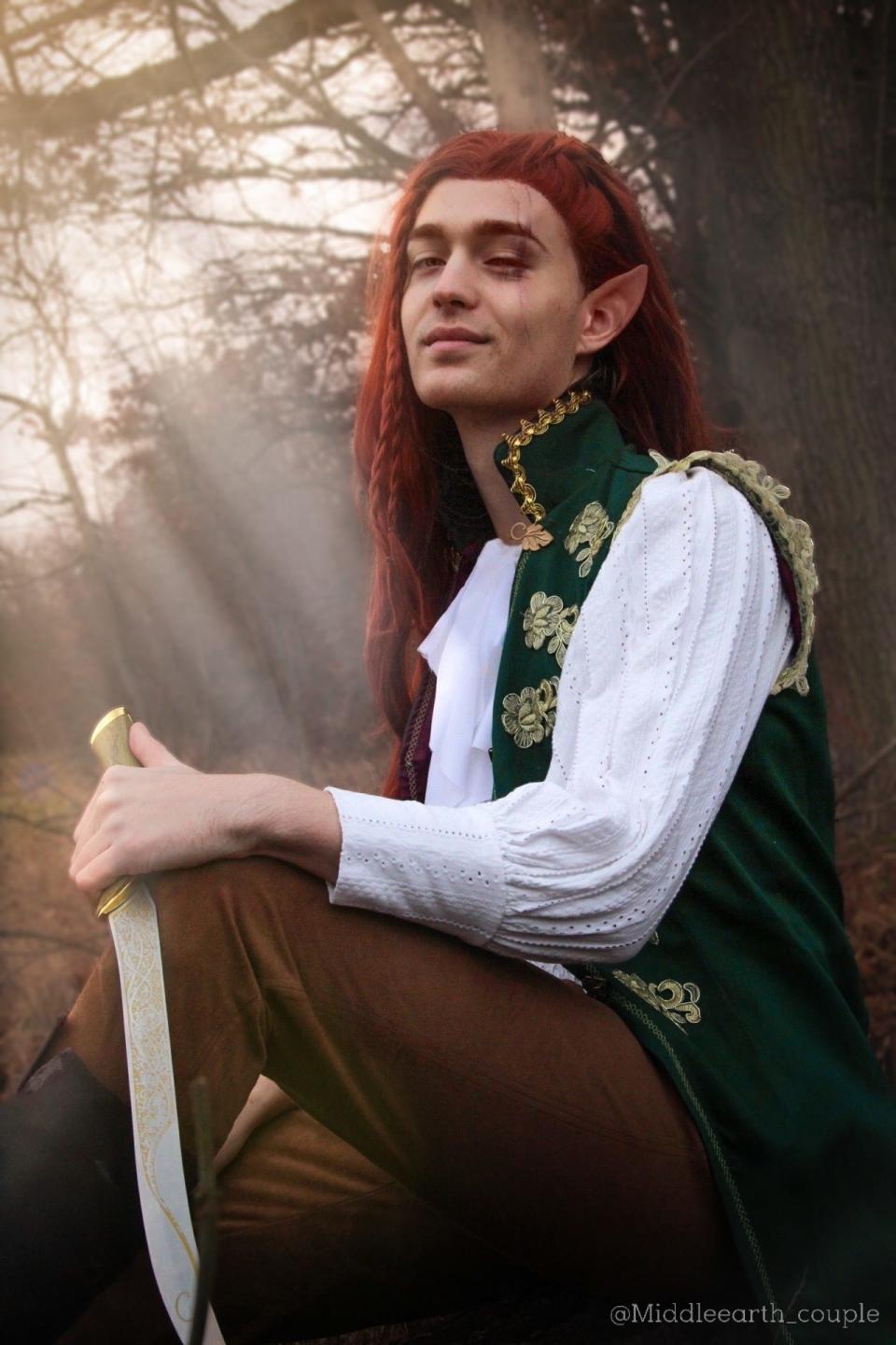 A man with a red wig sits on a rock with a sword.