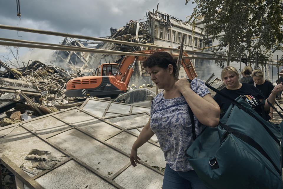 People carry their belongings as emergency service personnel work at the site of a destroyed building after a Russian attack in Odesa, Ukraine, Thursday, July 20, 2023. (AP Photo/Libkos)