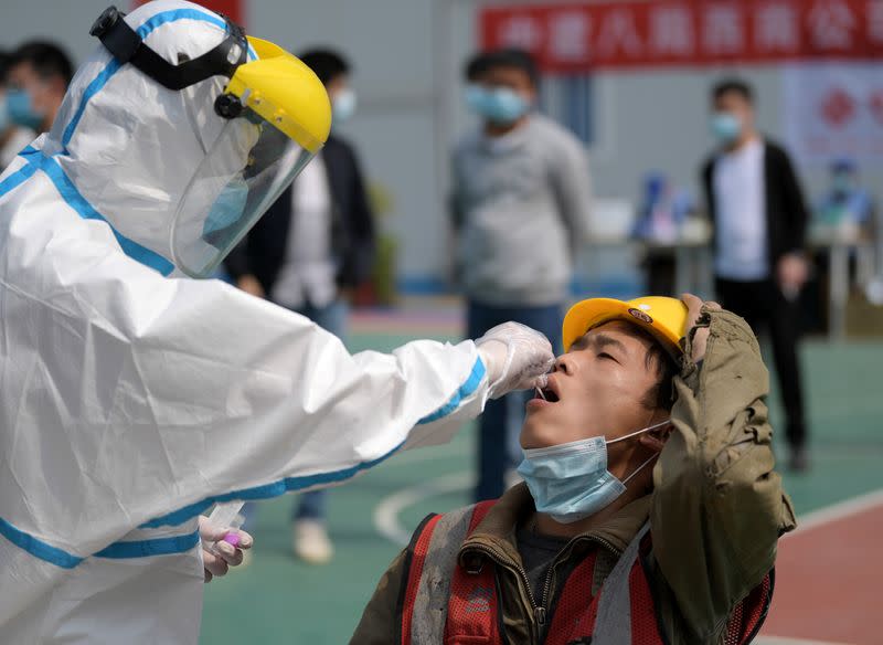 Worker in protective suit collects a swab from a construction worker for nucleic acid test in Wuhan