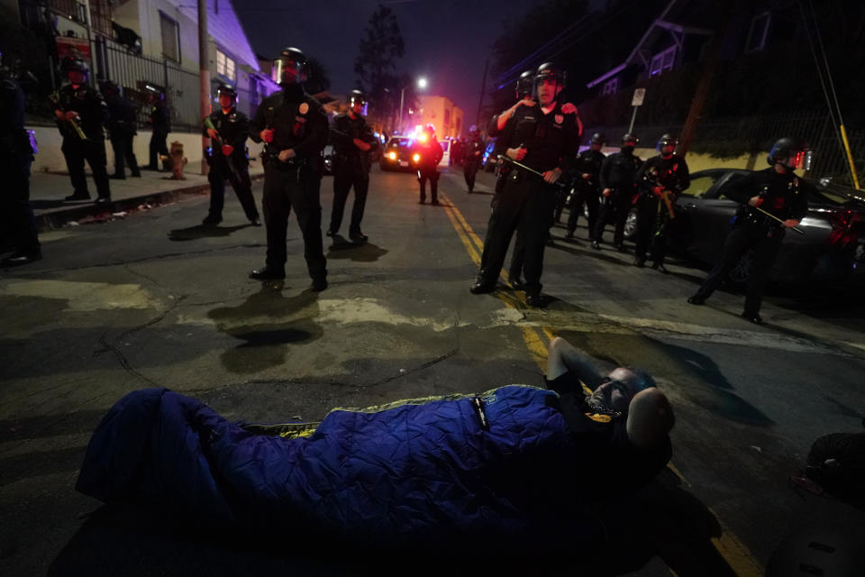 A demonstrator sets up a sleeping bag in front of police in the Echo Park section of Los Angeles Thursday, March 25, 2021. Demonstrators gathered Wednesday night to protest the planned temporary closure of a Los Angeles park that would displace a large homeless encampment, which has grown throughout the coronavirus pandemic. (AP Photo/Marcio Jose Sanchez)