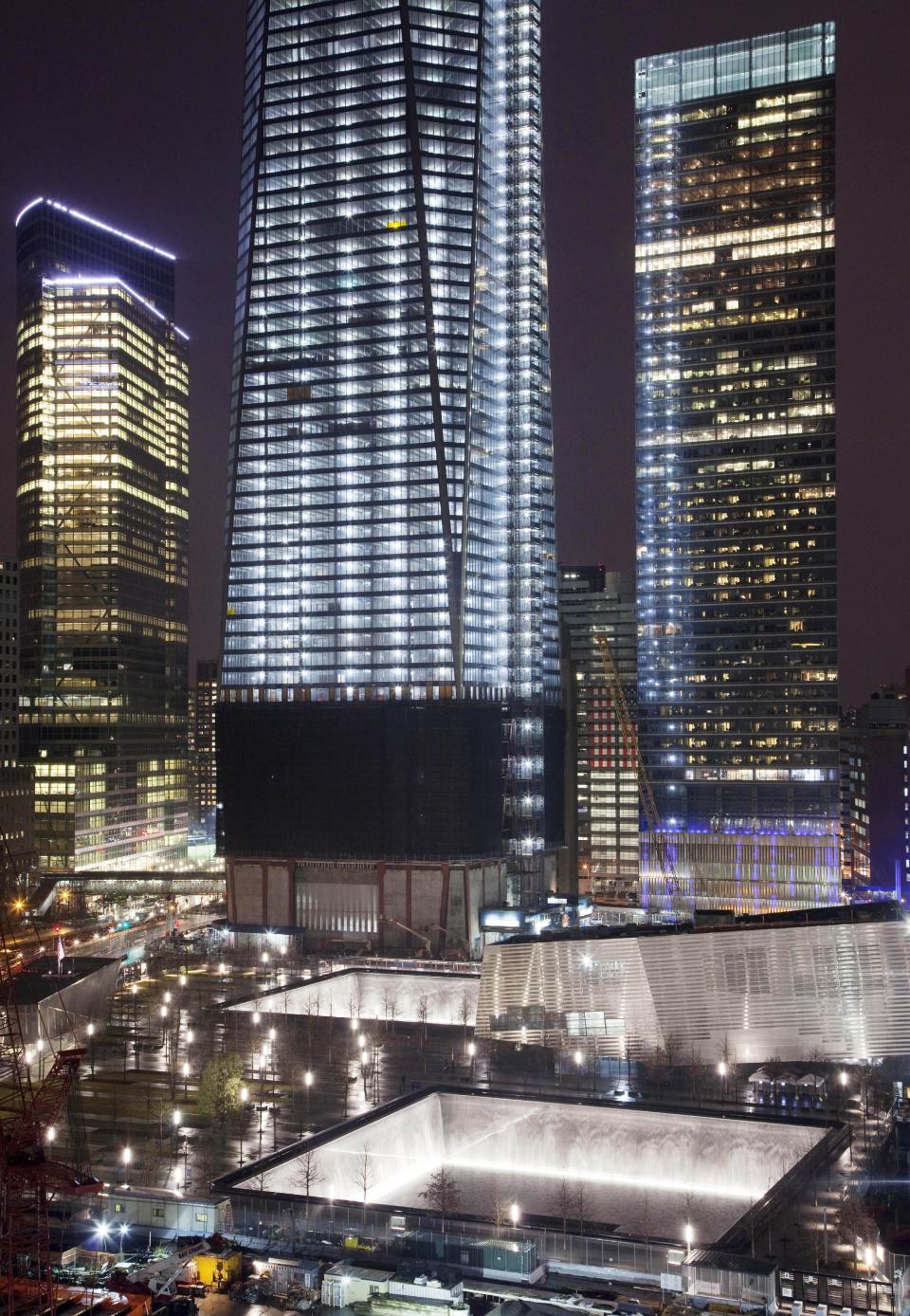 The twin reflecting pools, lower center, of the National September 11 Memorial are illuminated Sunday evening, April 1, 2012 at the World Trade Center in New York. One World Trade Center, center, is now up to 100 floors and will top out at 104 floors. (AP Photo/Mark Lennihan)