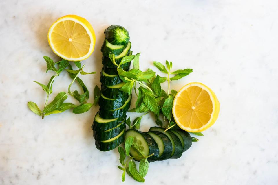 directly above shot of sliced cucumber and lemon with mint on white marble