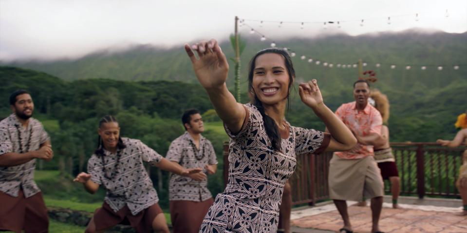 A group of people dancing in traditional attire at an outdoor gathering with festive lights and green hills in the background