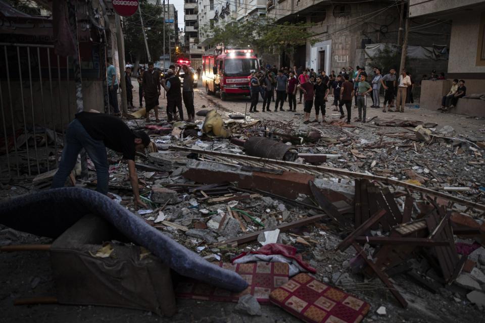 A man bends down to pick up something from the debris-strewn ground