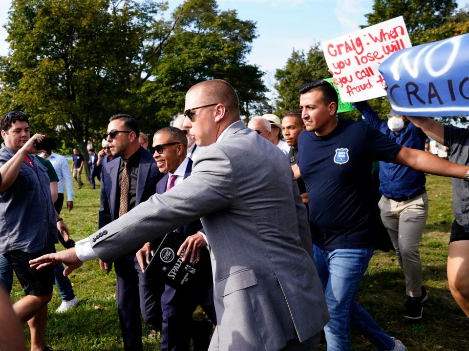 A security detail escorts former Detroit Police Chief James Craig from protesters before he could officially announce his run for Michigan governor as a Republican candidate on Sept. 14, 2021 from Belle Isle.