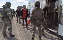 In this photo taken from video released by the Russian Defense Ministry Press Service on Tuesday, May 17, 2022, Russian servicemen watch Ukrainian servicemen boarding a bus as they are being evacuated from the besieged Azovstal steel plant in Mariupol, Ukraine. More than 260 fighters, some severely wounded, were pulled from a steel plant on Monday that is the last redoubt of Ukrainian fighters in the city and transported to two towns controlled by separatists, officials on both sides said. (Russian Defense Ministry Press Service via AP)
