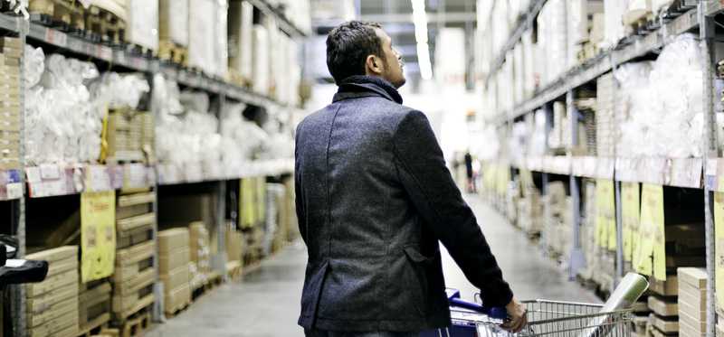 A man shops in a warehouse store with a cart.