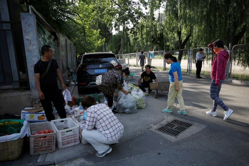 Street vendors sell vegetables and fruits at a stall by a river near a residential area in Beijing