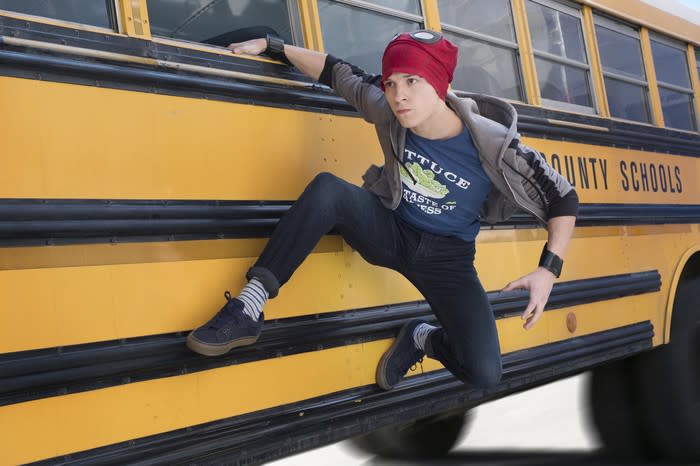 A teenager hanging from the window of a moving school bus.