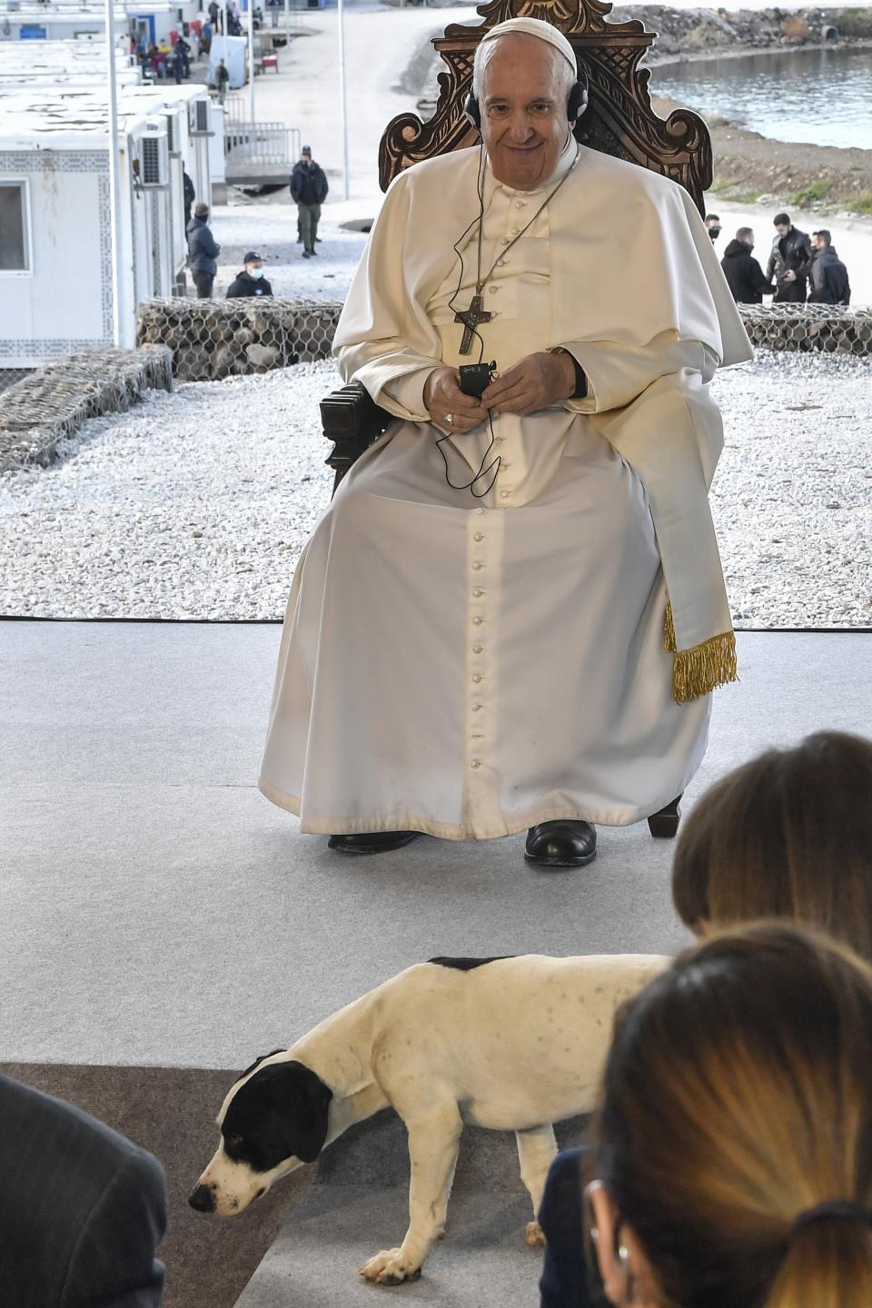 Pope Francis smiles as a dog passes in front of him during a ceremony at the Karatepe refugee camp, on the northeastern Aegean island of Lesbos, Greece, Sunday, Dec. 5, 2021. Pope Francis returned Sunday to the Greek island of Lesbos to offer comfort to migrants at a refugee camp and blast what he said was the indifference and self-interest shown by Europe "that condemns to death those on the fringes." (Louisa Gouliamaki/Pool via AP)