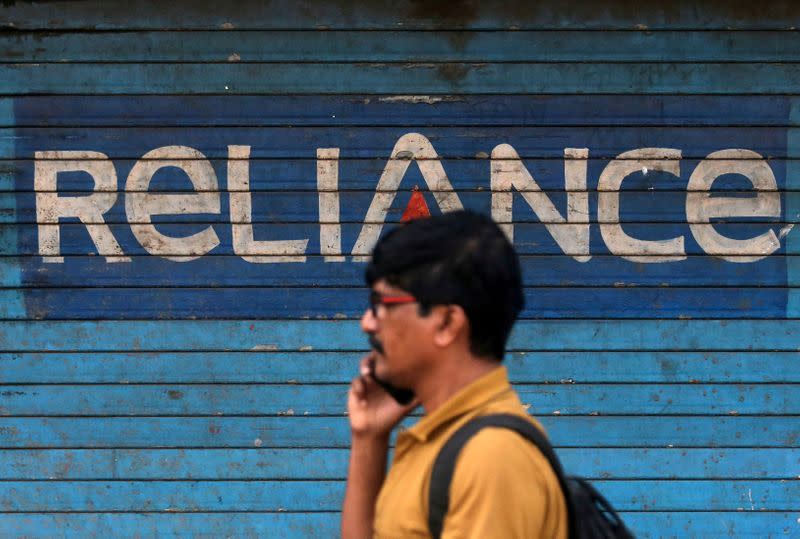 FILE PHOTO: A man speaks on his mobile phone as he walks past a closed shop painted with an advertisement of Reliance Communications in Mumbai