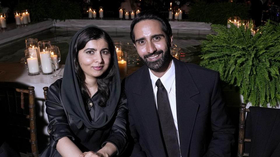 malala yousafzai sitting behind a table and smiling alongside husband asser malik