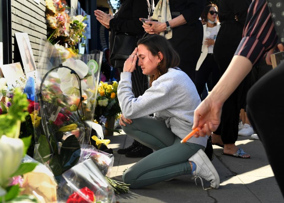 A woman kneels before memorial.