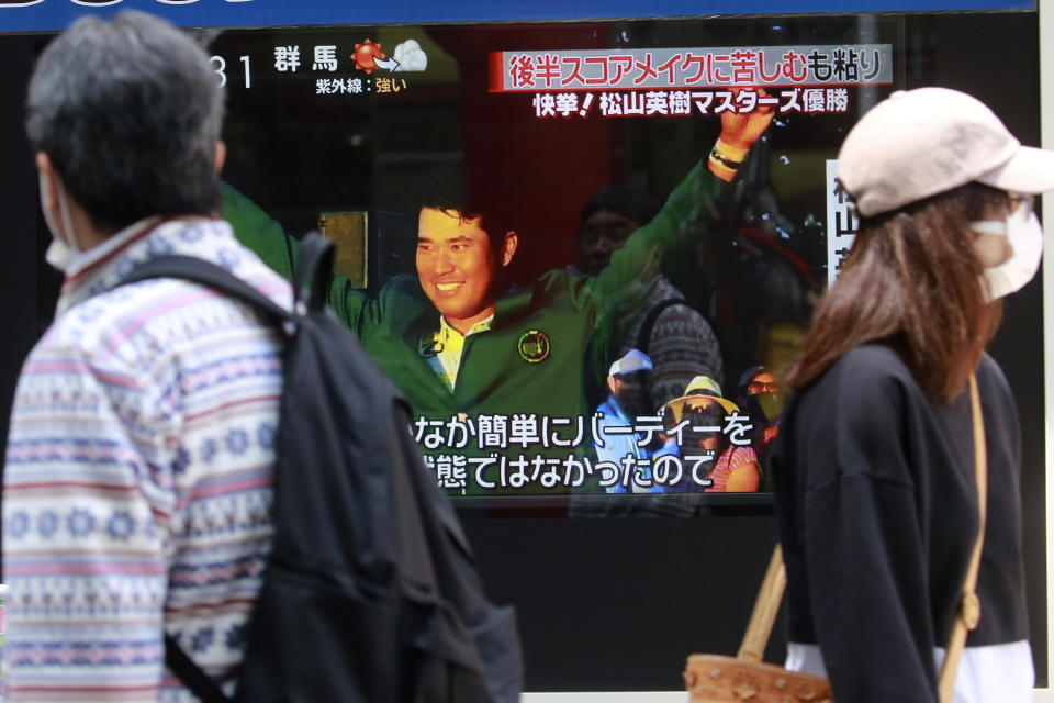 People walk past Japanese golfer Hideki Matsuyama seen in a TV news channel reporting his win in the Masters golf tournament, in Tokyo, Monday, April 12, 2021. From Japan's prime minister on down, the country celebrated Matsuyama's victory in the Masters — the first Japanese to win at Augusta National and wear the famous green jacket.(AP Photo/Koji Sasahara)