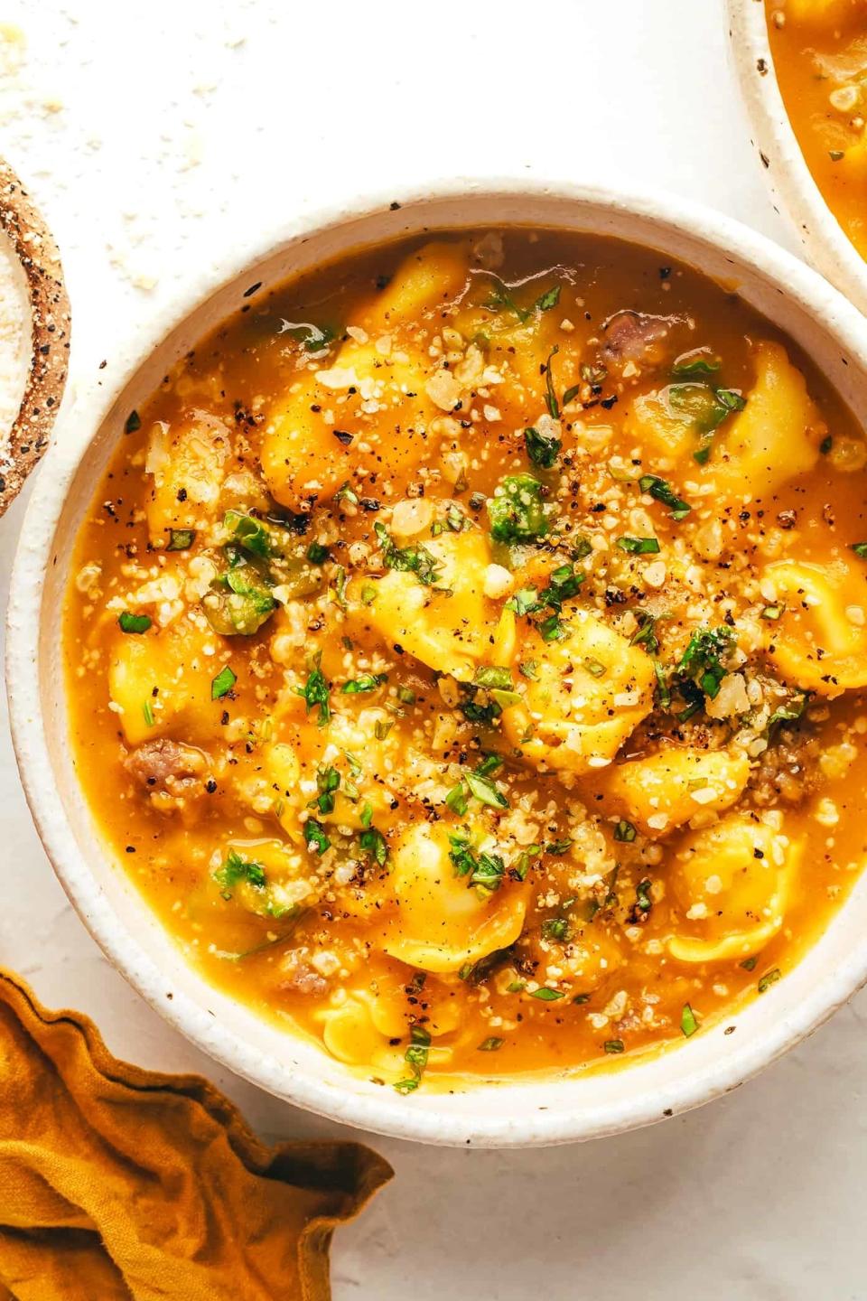 a bowl of butternut squash tortellini soup served with fresh herbs