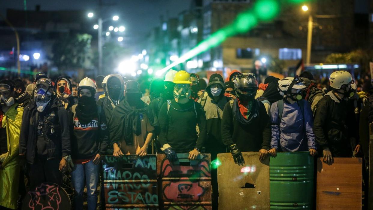 Demonstranten stehen bei einem Protest an einer Kreuzung mit Schildern und Laserpointern.