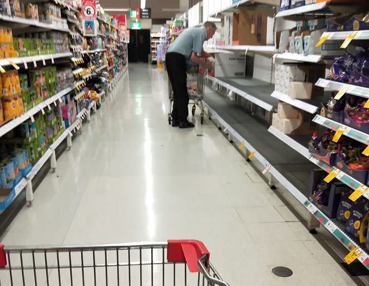 An elderly man searches a Coles aisle in Perth for toilet paper.