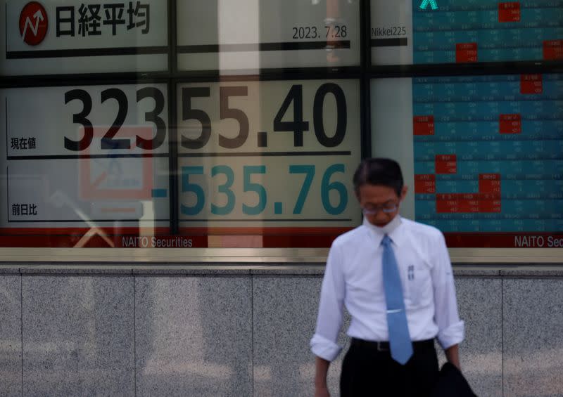 FILE PHOTO: A man stands in front of an electric board displaying the Nikkei stock average outside a brokerage in Tokyo