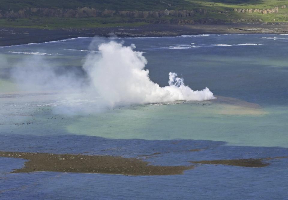 In this aerial photo, plume billows from the water off the Ioto island, seen rear, following an eruption in Ogasawara, southern Tokyo, Japan, on Oct. 30, 2023. An unnamed undersea volcano, located about 1 kilometer (half a mile) off the southern coast of Iwo Jima, which Japan calls Ioto, started its latest series of eruptions on Oct. 21. (Kyodo News via AP)