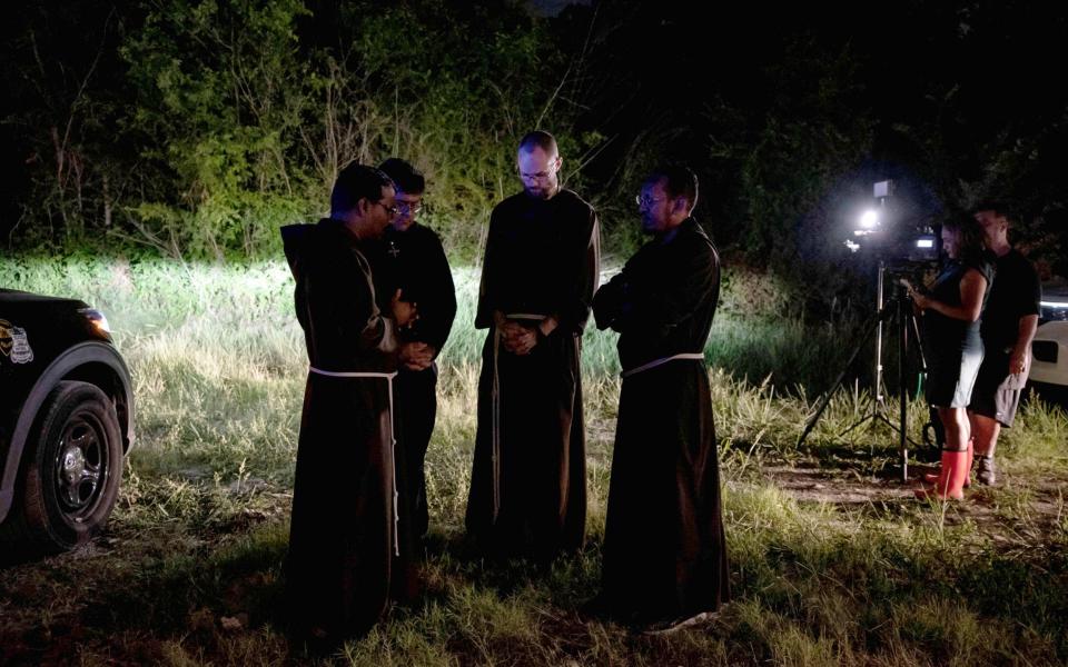 Local priests from the San Antonio Archdiocese stand nearby, praying - SERGIO FLORES 