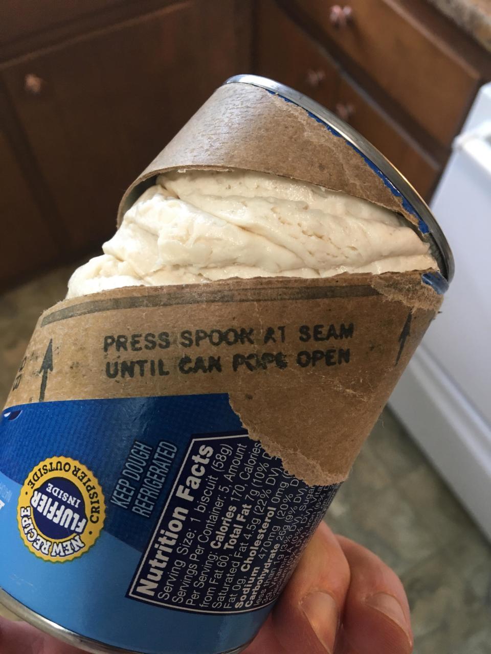 Person holding a peeled-open canned Pillsbury biscuits with contents partially visible