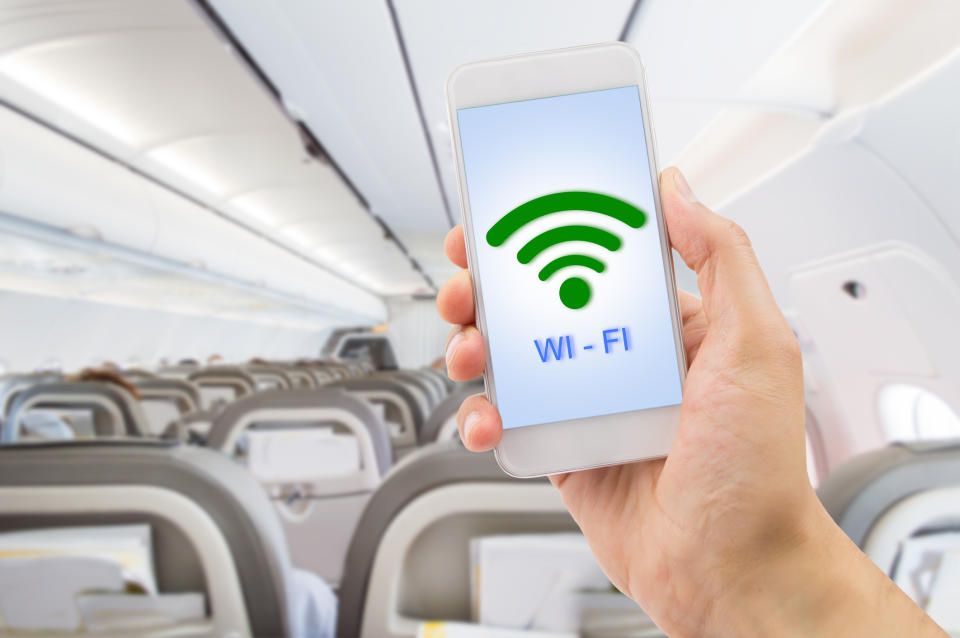 A man holding up a smartphone with the word and icon for Wi-Fi on the screen while inside an airplane.