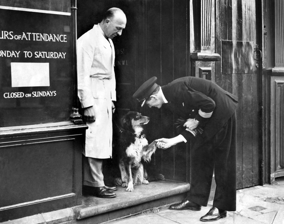 A black and white photo shows a ship captain shaking hands with the boat's mascot in 1942.