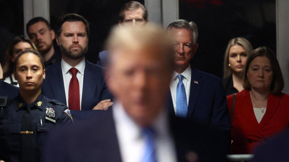 PHOTO: Senator J.D. Vance (left, red tie)(R-OH) looks on as former US President Donald Trump speaks to the media at his trial for allegedly covering up hush money payments at Manhattan Criminal Court, in New York City, on May 13, 2024.  (Spencer Platt/POOL/AFP via Getty Images)
