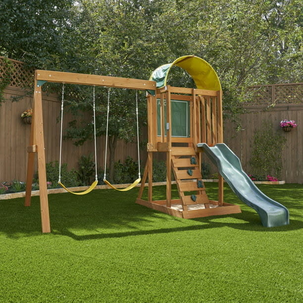 Outdoor wooden playset with swings, slide, and climbing wall in a backyard