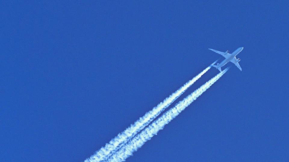 Am blauen Himmel fliegt ein Flugzeug und hinterlässt Kondensstreifen.