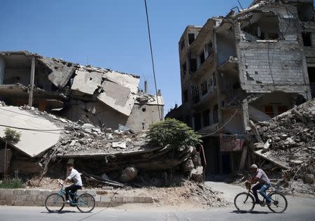 Syrian men ride their bicycles at the rebel held besieged Douma neighbourhood of Damascus, Syria July 23, 2017. REUTERS/Bassam Khabieh