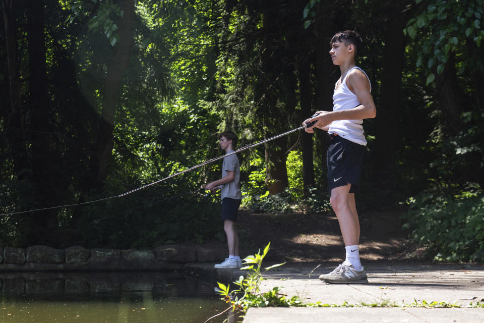 Michael Schoeb, left, and his friend Jack Guatelo, right, fish at Lake Emile in Reniehausen Park in McKeesport, Pa, on Monday, June 17, 2024. The two fisherman stayed safe from the heat by standing in the shade. (Esteban Marenco/Pittsburgh Post-Gazette via AP)