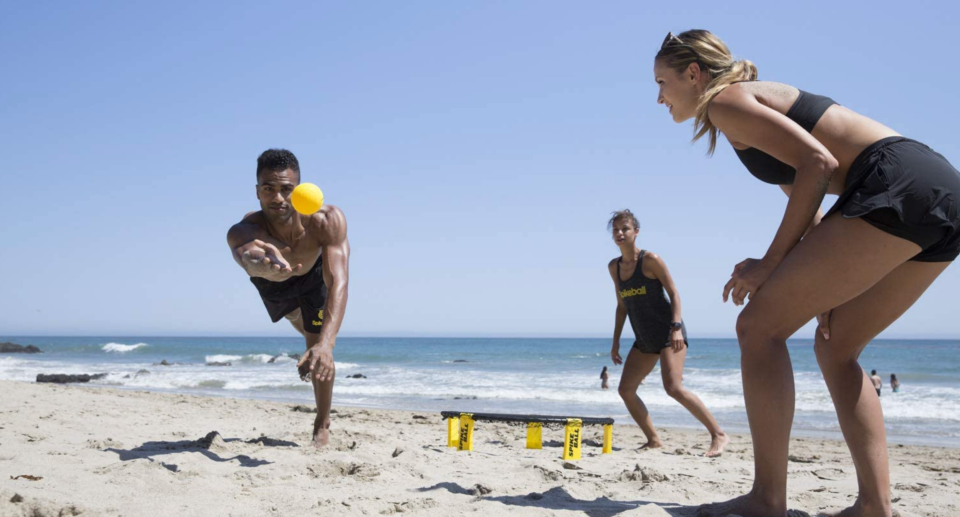 three players playing spikeball on beach, spikeball game