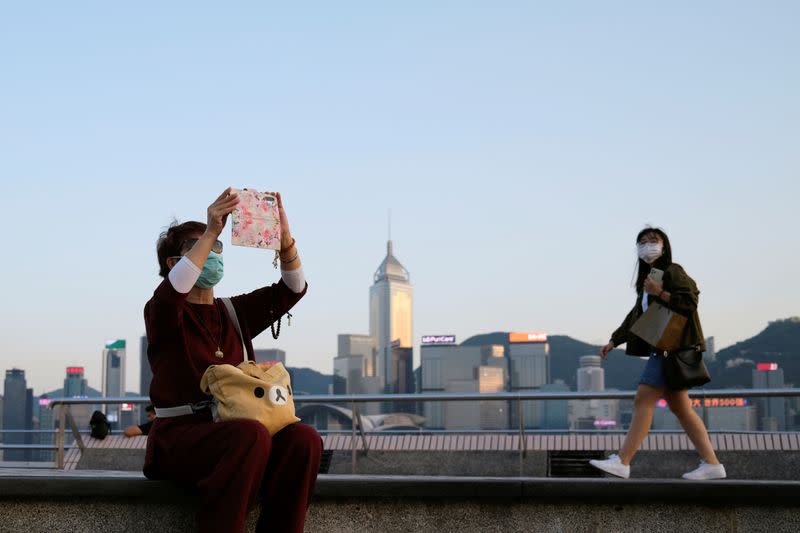 FILE PHOTO: People with protective masks walk in front of Hong Kong's skyline