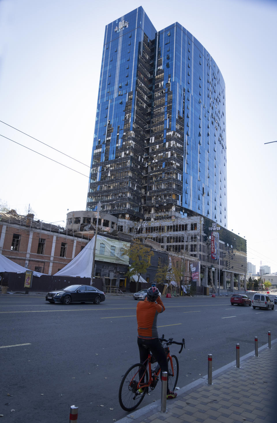 A cyclist takes a photo of an office center and a building damaged in a Russian rocket attack a week ago, in central Kyiv, Ukraine, Sunday, Oct. 16, 2022. (AP Photo/Efrem Lukatsky)