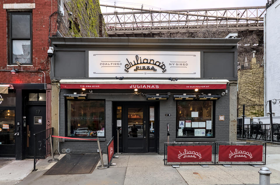 Exterior view of Juliana's Pizza under a bridge, with signage, outdoor seating, and dual entrance doors