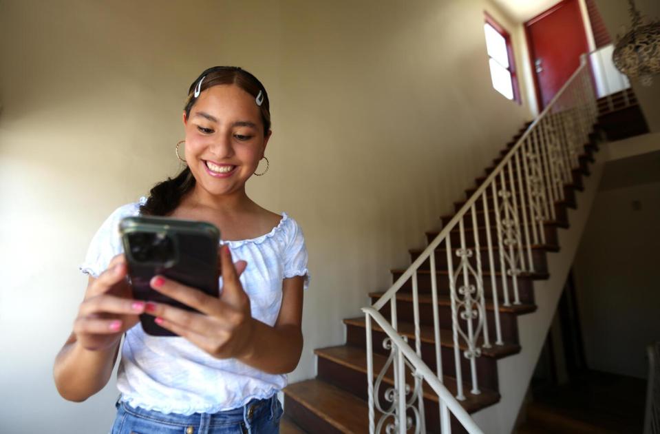 A teen girl stands on a staircase looking at her cellphone and smiling