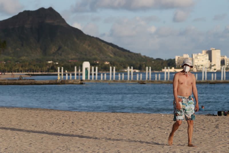 FILE PHOTO: A beachgoer wearing a protective mask walks down Waikiki Beach, with Diamond Head mountain in the background