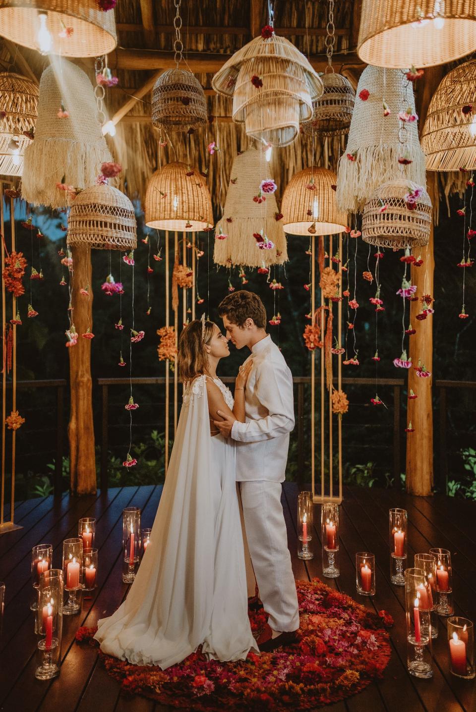 A bride and groom look at each other in a room full of flowers and candles.