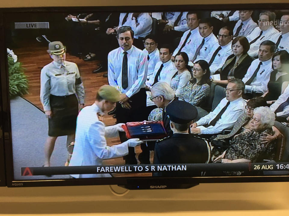 A member of the Coffin Bearer Party hands over the Singapore flag and accoutrements S R Nathan’s casket to President Tony Tan Keng Yam. These were then handed over to Nathan’s son Osith (standing). (Photo: TV screenshot)