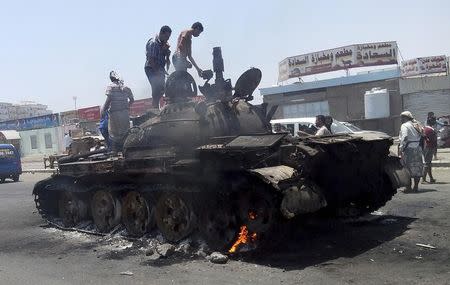 People stand on a tank that was burnt during clashes on a street in Yemen's southern port city of Aden March 29, 2015. REUTERS/Stringer